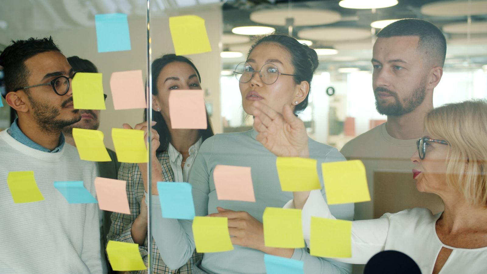 A diverse group of adults brainstorming with sticky notes in a modern office.